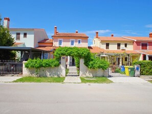 Una hilera de casas con entrada protegida por un portón, cielo despejado y calle pavimentada.