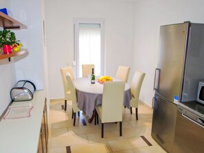 Cocina compacta con una mesa de comedor preparada para cuatro personas, un refrigerador y un microondas.