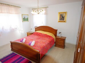 Ein Schlafzimmer mit einem hölzernen Bett, zwei Nachttischen, einem Beistelltisch, einer Deckenleuchte und zwei gerahmten Bildern an der Wand.