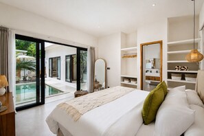 A modern bedroom with a large bed, a glass door leading to a pool, and a bathroom with a mirror and shelves.