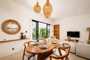 A dining area with a round table set for four, a large mirror, and a television on the wall.