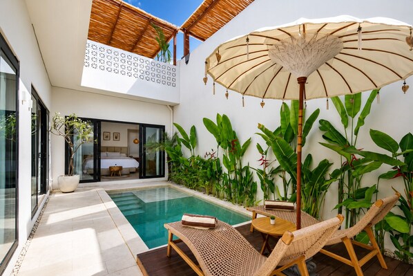 A private pool area with a lounge chair, a table, and an umbrella.