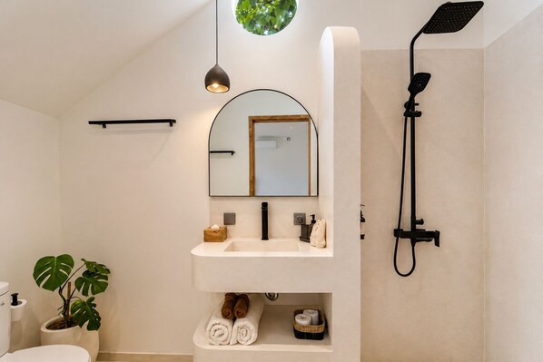 A modern bathroom with a freestanding sink, a showerhead, a mirror, and a potted plant.