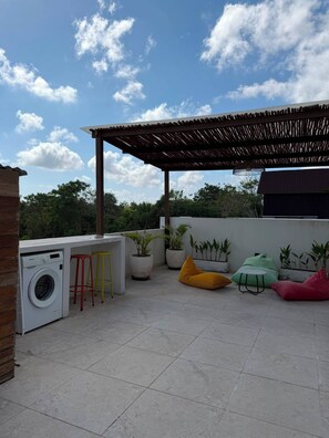 Une terrasse sur le toit équipée d’un lave-linge, de tabourets de bar, de plantes en pot et d’une pergola.