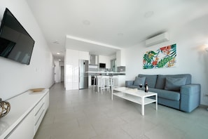 Una sala de estar moderna con un sofá gris, una mesa de centro blanca y un televisor de pantalla plana montado en la pared.