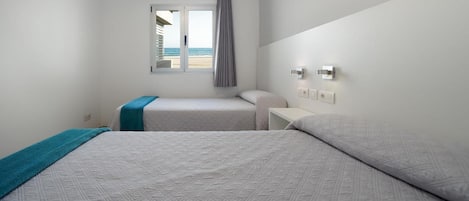 Een hotelkamer met twee bedden, een raam met uitzicht op het strand, een nachtkastje en een wandlamp.