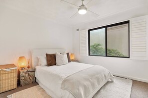 Ein Schlafzimmer mit einem Bett, zwei Nachttischen, einem Deckenventilator und einem Fenster mit Rollläden.