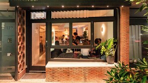 En restaurant med facade i mursten, store vinduer og indendørs siddepladser, som kan ses gennem glasset.