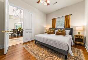 A bedroom with a bed, bedside tables, a rug, a window with curtains, and a door leading to a dining area. - Lakefront 7BR, 7BA Retreat with Pool, Hot tub, Game room, and Private dock. (Hot Springs)