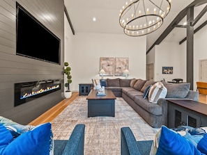 Een moderne woonkamer met een open haard, een grote flatscreen televisie en een hoekbank.