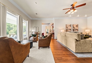 A spacious living room with a high ceiling, a ceiling fan, and a view of the outdoors through large windows. - Lakefront 7BR, 7BA Retreat with Pool, Hot tub, Game room, and Private dock. (Hot Springs)