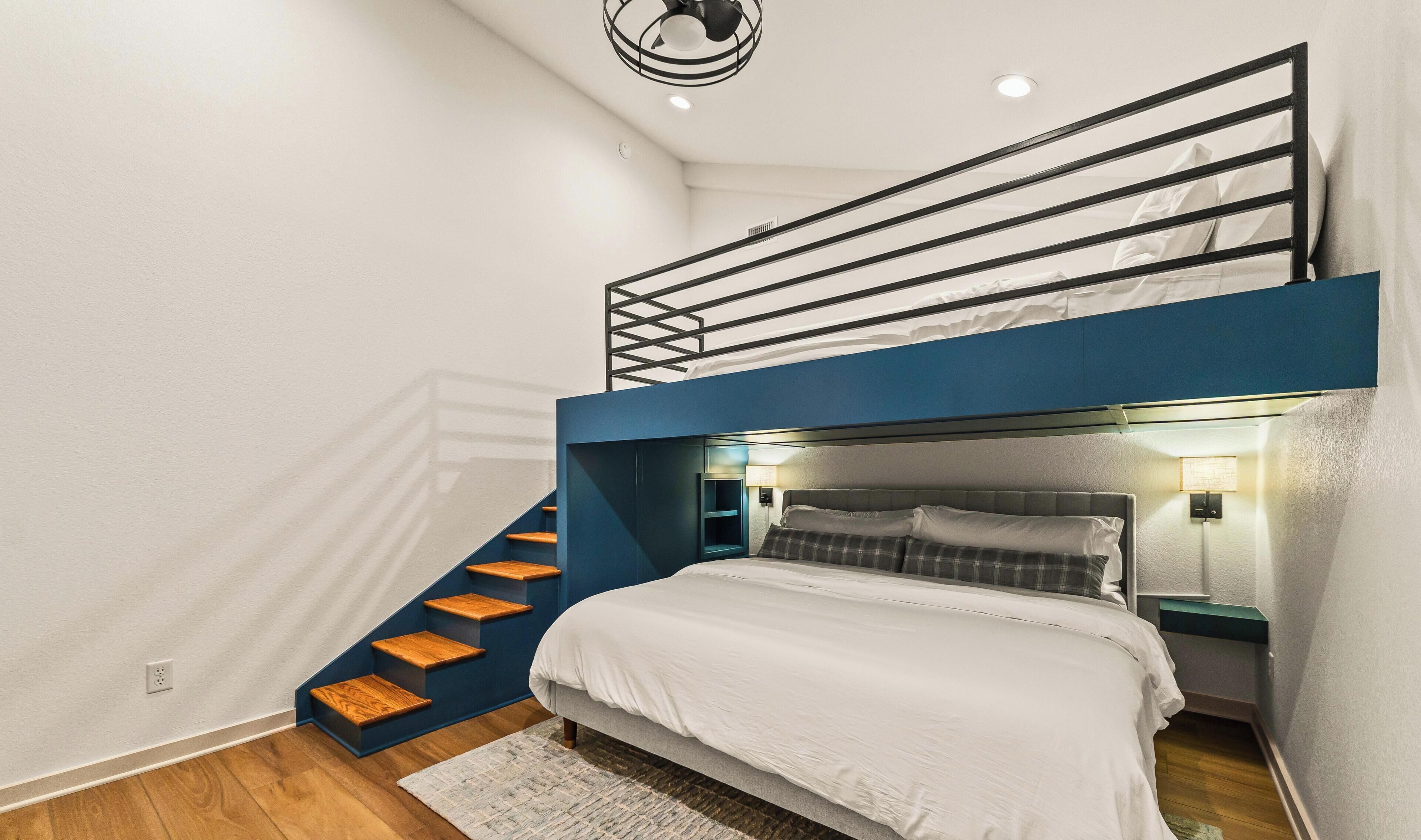 Un lit superposé avec un bureau et une chaise, un petit escalier et un luminaire fixé au mur.