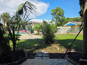 A residential outdoor area with a paved driveway, a small garden, and a fenced tennis court. - Coral Cottage! Steps to Pool From Back Door! (Panama City Beach)