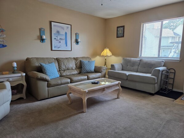 A living room with two sofas, a coffee table, a lamp, and wall decorations. - Coral Cottage! Steps to Pool From Back Door! (Panama City Beach)