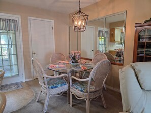 A dining area with a glass table, wicker chairs, a floral centerpiece, and a hanging light fixture. - Coral Cottage! Steps to Pool From Back Door! (Panama City Beach)