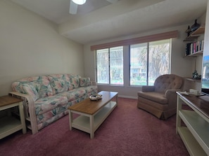A living room with a floral sofa, a wooden coffee table, a brown armchair, and a bookshelf. - Coral Cottage! Steps to Pool From Back Door! (Panama City Beach)