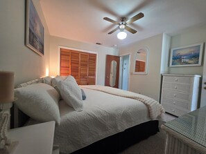 A bedroom with a bed, a ceiling fan, a dresser, and a door. - Coral Cottage! Steps to Pool From Back Door! (Panama City Beach)