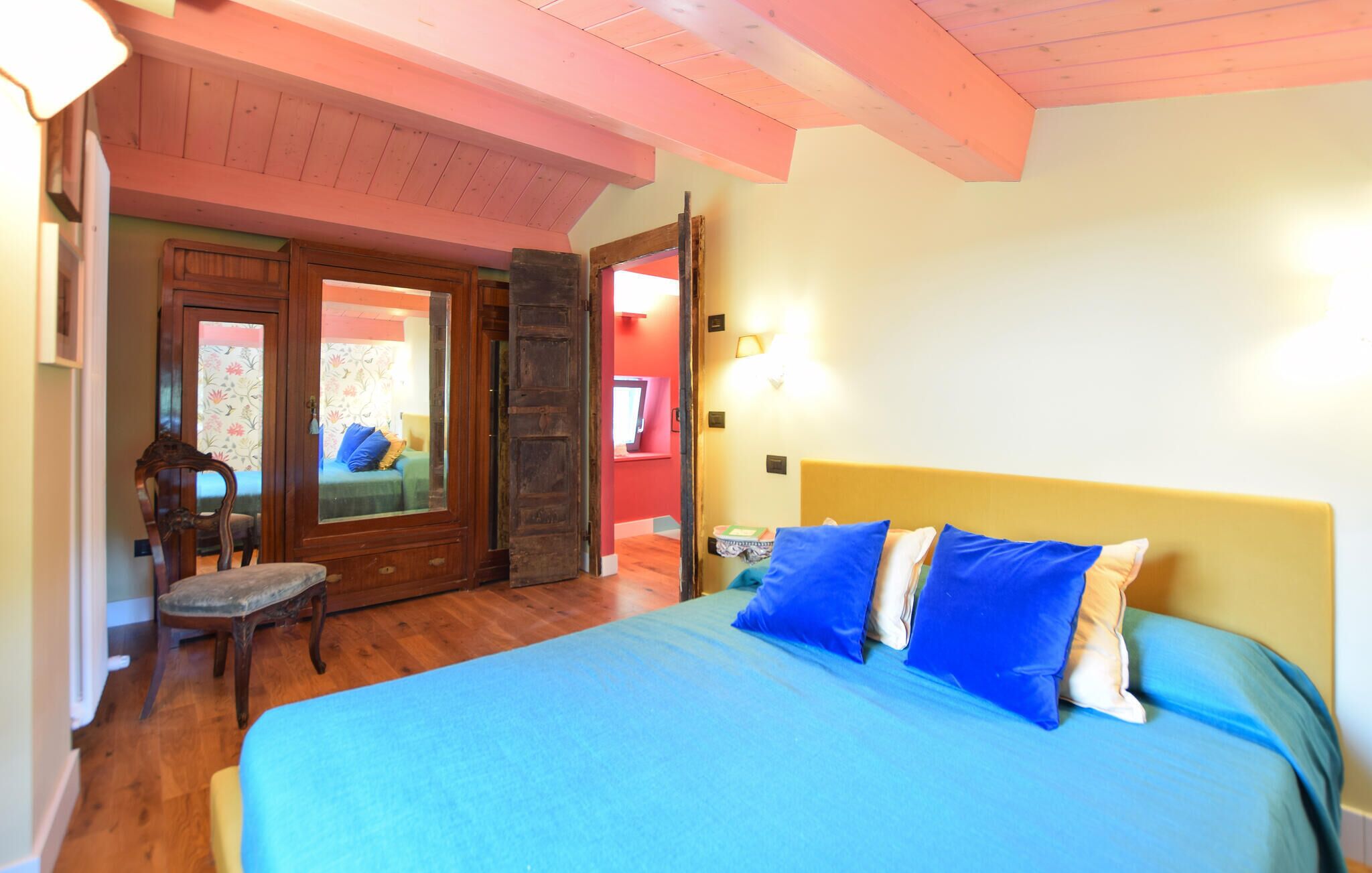 Ein Schlafzimmer mit einem Bett, einem Sessel, einer Holztür und einer Wandleuchte.