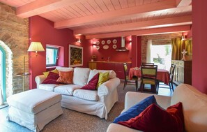Un salon confortable avec un canapé, un pouf et des fauteuils, un coin repas avec une table et des chaises, et une cuisine avec une fenêtre.