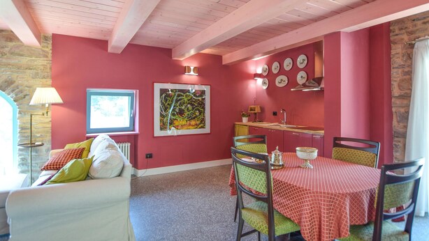 Uma área de refeições com uma mesa posta para dois, um sofá com almofadas, uma janela com vista e uma parede decorada com pratos.