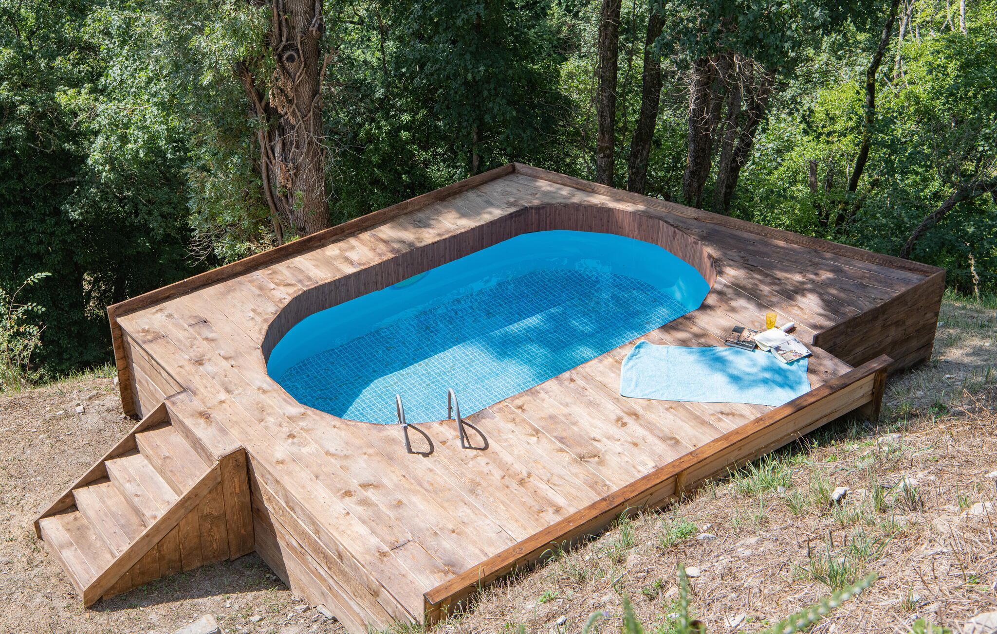A wooden deck with a built-in swimming pool, steps leading into the pool, and a towel and sunglasses on the deck.