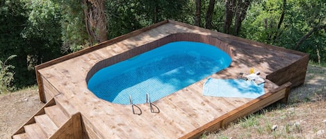 A wooden deck with a built-in swimming pool, steps leading into the pool, and a towel and sunglasses on the deck.