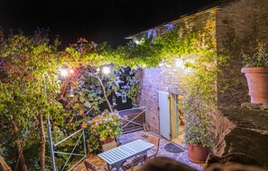 A stone building with a wooden table and chairs outside, surrounded by greenery and string lights. - 1 bedroom lovely home in Badia Tedalda, Loc. Ac (Badia Tedalda, Loc. Ac)