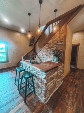 A rustic kitchen with a stone island, wooden bar stools, and a wooden staircase. - Spacious 5-bedroom house in peaceful Branson with AC (Branson)