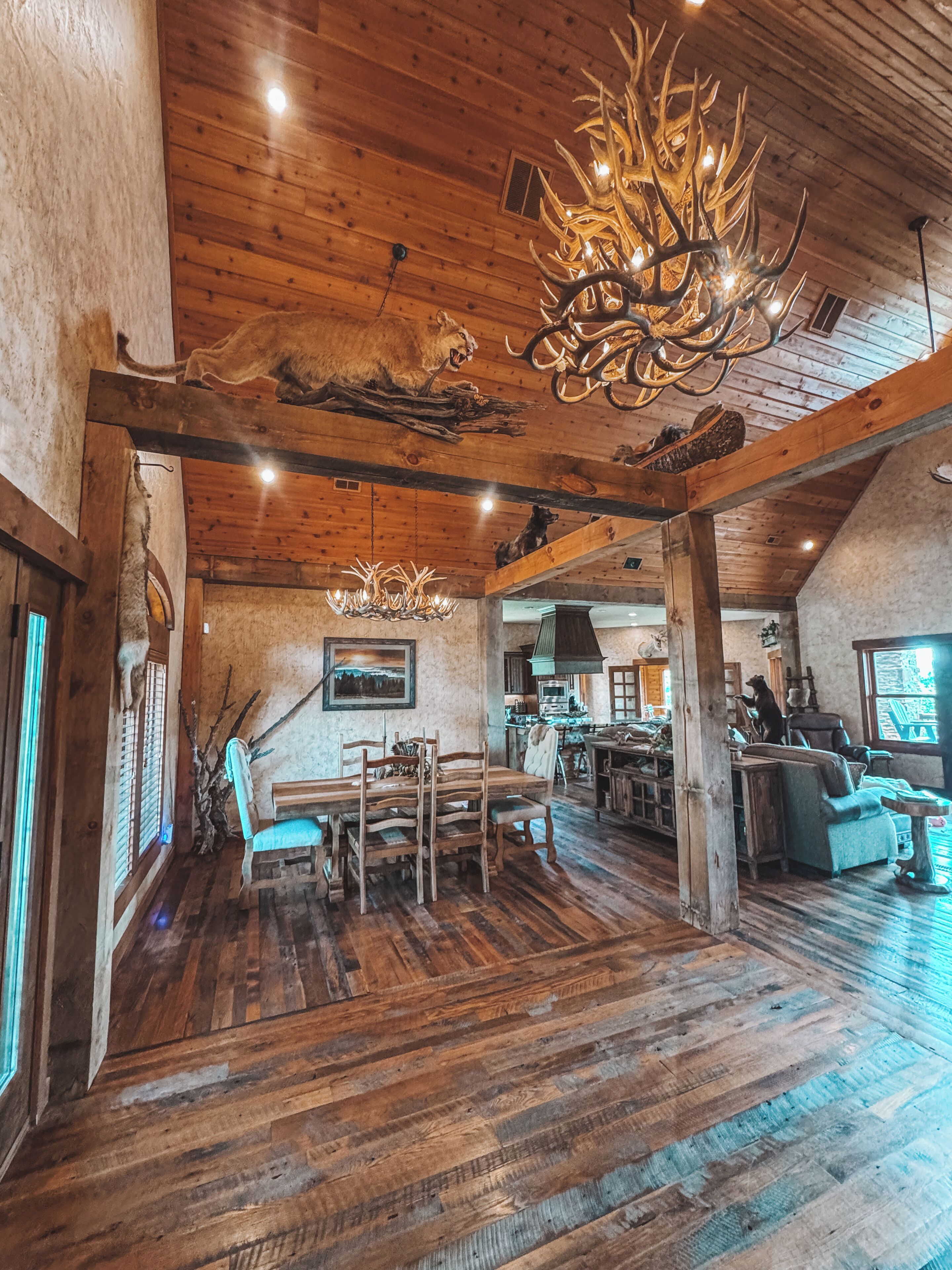 A spacious interior with a high ceiling, wooden beams, and a dining area with multiple chairs and a table.