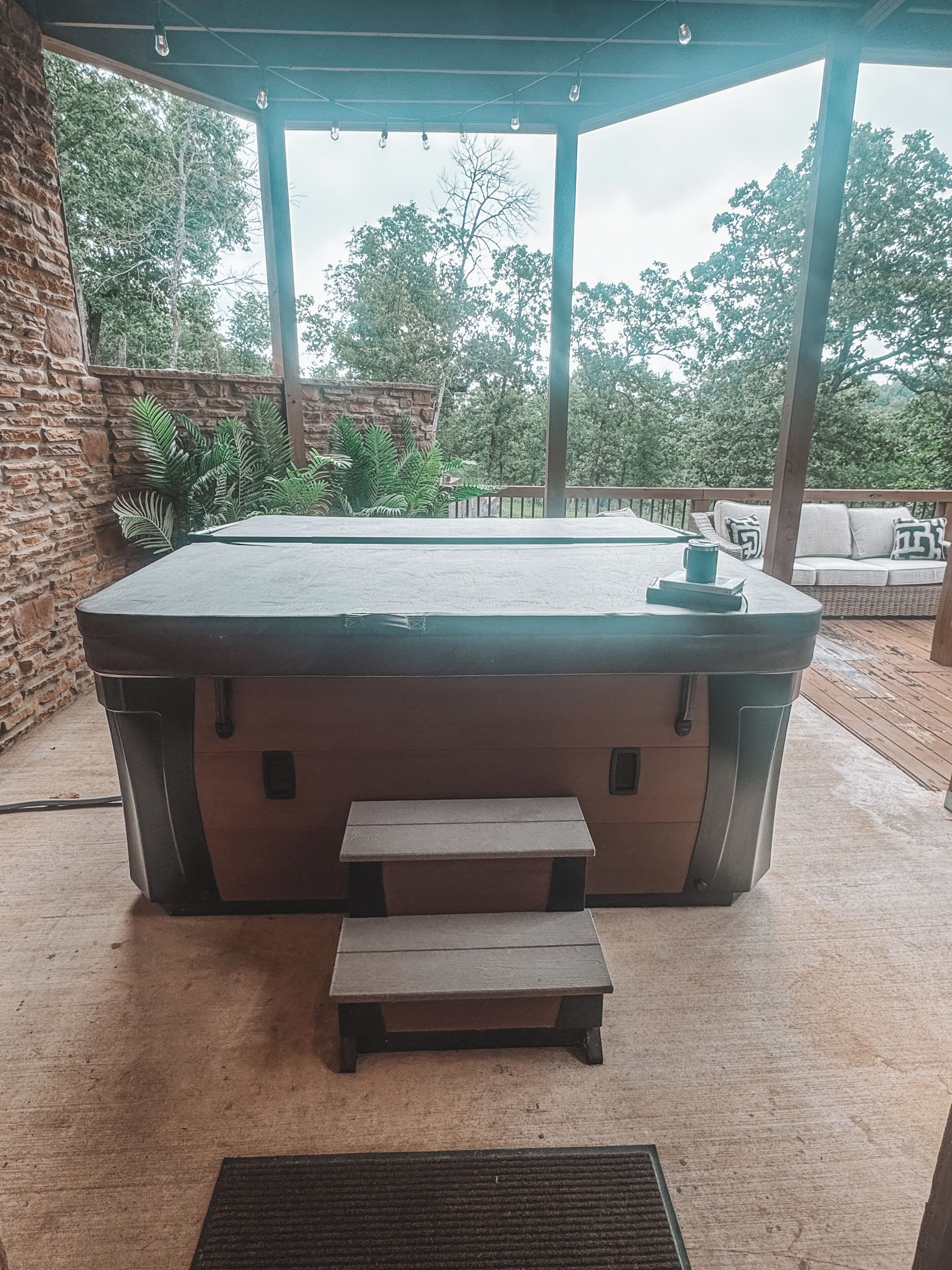 Un jacuzzi con escalones de acceso, rodeado por una terraza de madera y un muro de piedra.