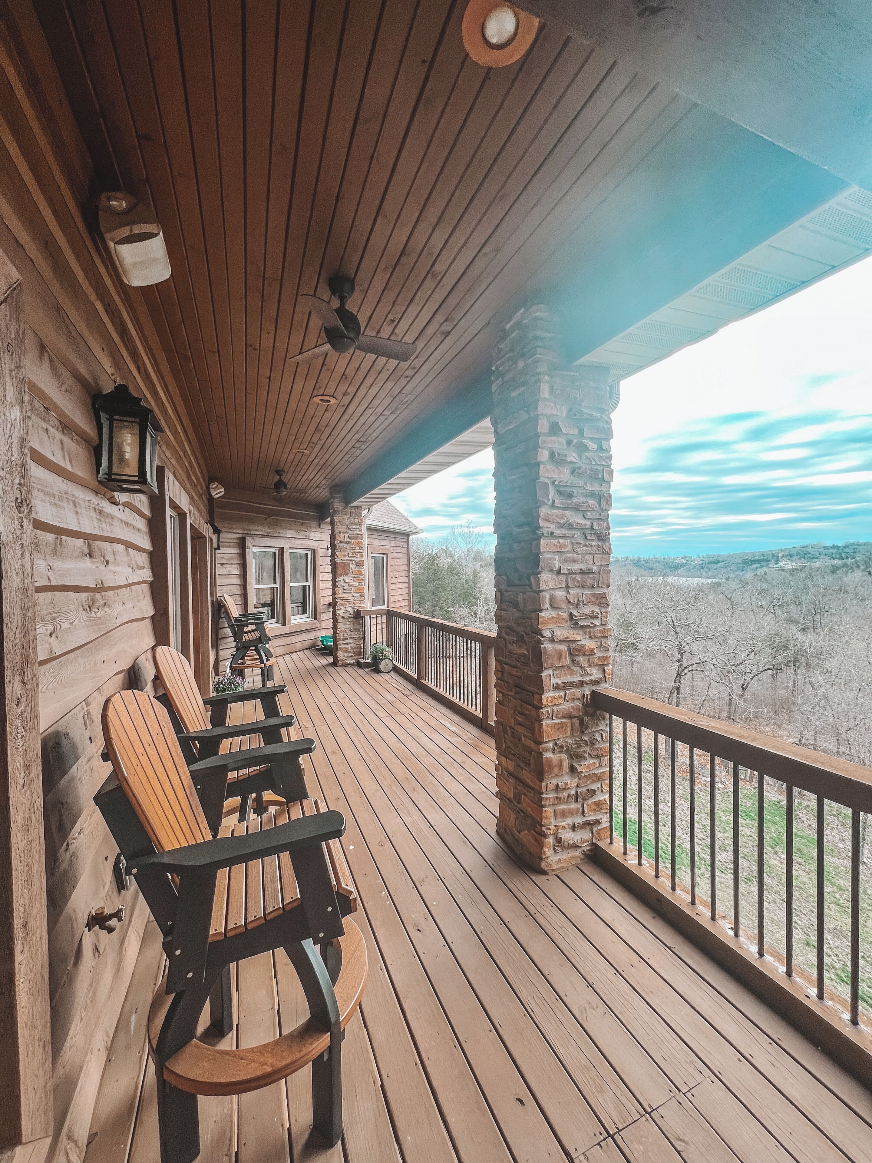 A wooden deck with Adirondack chairs, a stone pillar, and a view of the landscape.