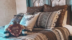 Una cama con una colcha estampada, varias almohadas, una caja con forma de corazón y una botella.