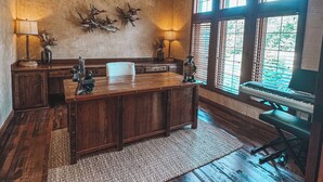 Una habitación amplia con un escritorio de madera, ventilador de techo y una ventana grande con persianas.