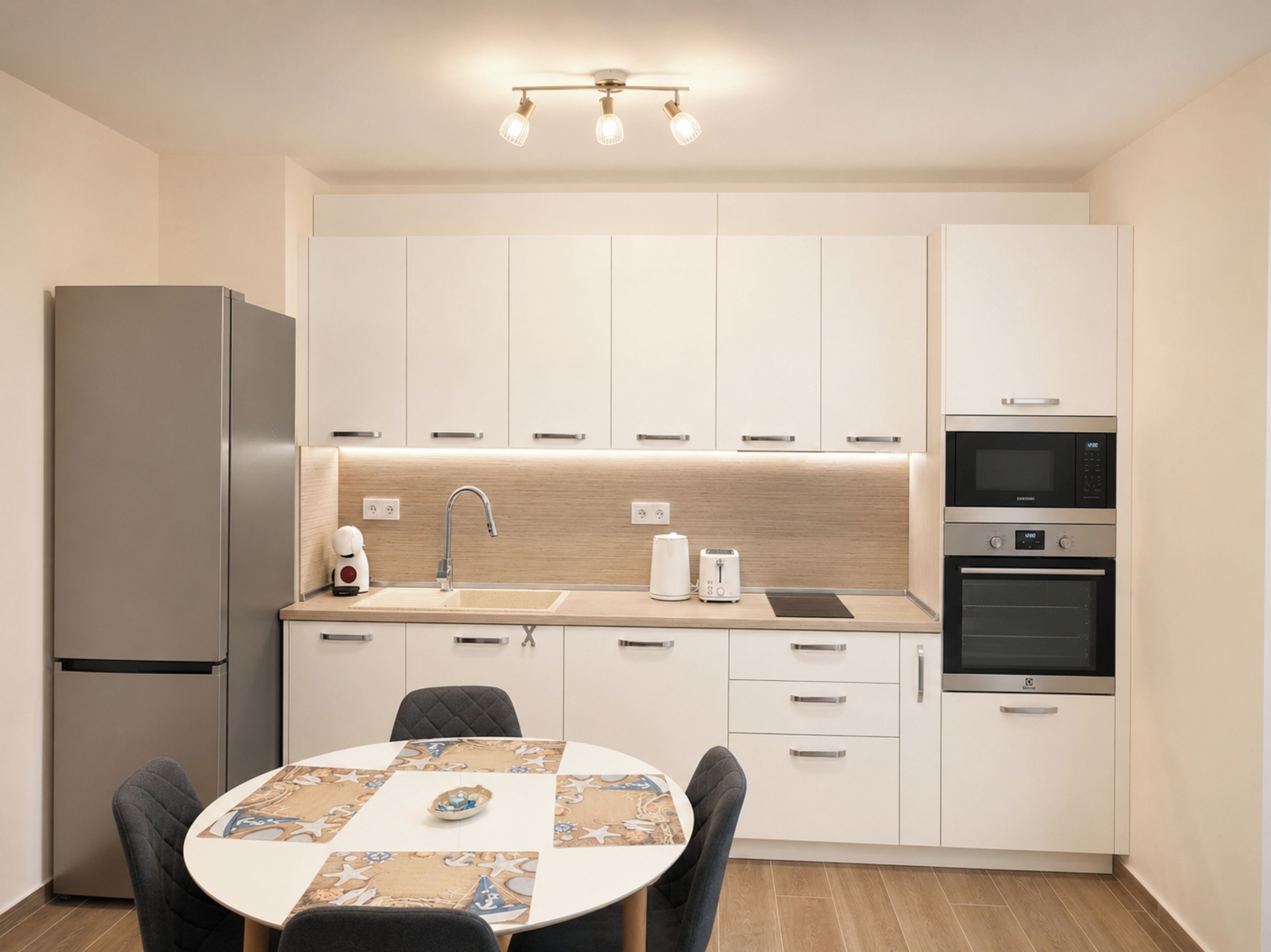 A modern kitchen with white cabinets, a stainless steel refrigerator, a sink, a toaster, and a microwave.