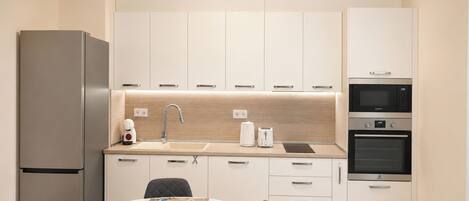A modern kitchen with white cabinets, a stainless steel refrigerator, a sink, a toaster, and a microwave.