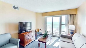 Ein Hotelzimmer mit Fernseher, einer Couch, einem Sessel, einem Tisch und Meerblick vom Balkon.