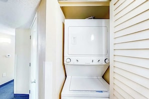 A laundry room with a stacked washer and dryer, a door leading to another room, and a window with blinds. - Carolinian Beach Resort 0430 (Myrtle Beach)