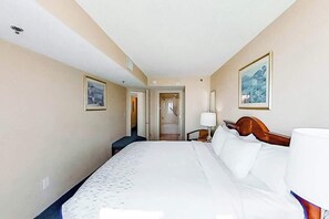 Une chambre d’hôtel avec un grand lit, une table de chevet avec une lampe et deux tableaux encadrés accrochés aux murs.
