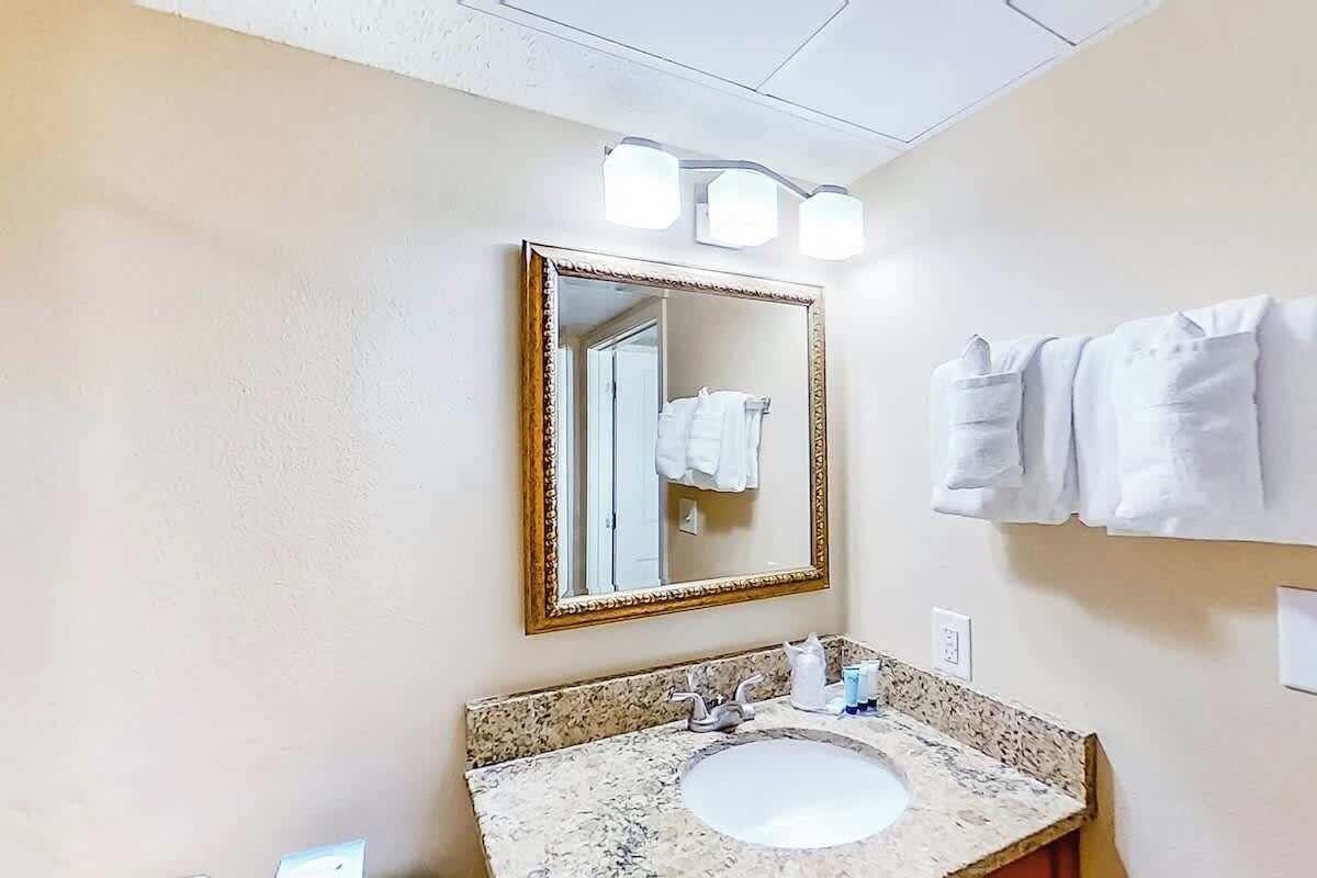 A bathroom with a granite countertop sink, a mirror with a gold frame, and a towel rack with white towels.