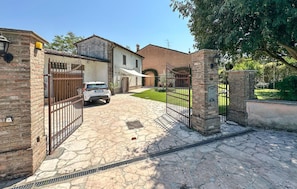 A gated property with a paved driveway, a white car parked in front, and a building with a tiled roof. - Stunning home in Goito with WiFi (Goito)