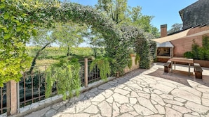 A stone patio with a pergola covered in greenery, a barbecue area, and a bench.