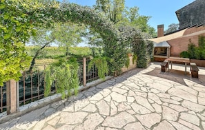 A stone patio with a pergola covered in greenery, a barbecue area, and a bench.