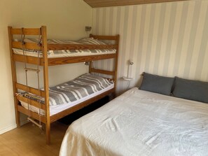 Ein Etagenbett mit Kopfstütze, ein Nachttisch mit Lampe und ein Einzelbett mit Kissen.