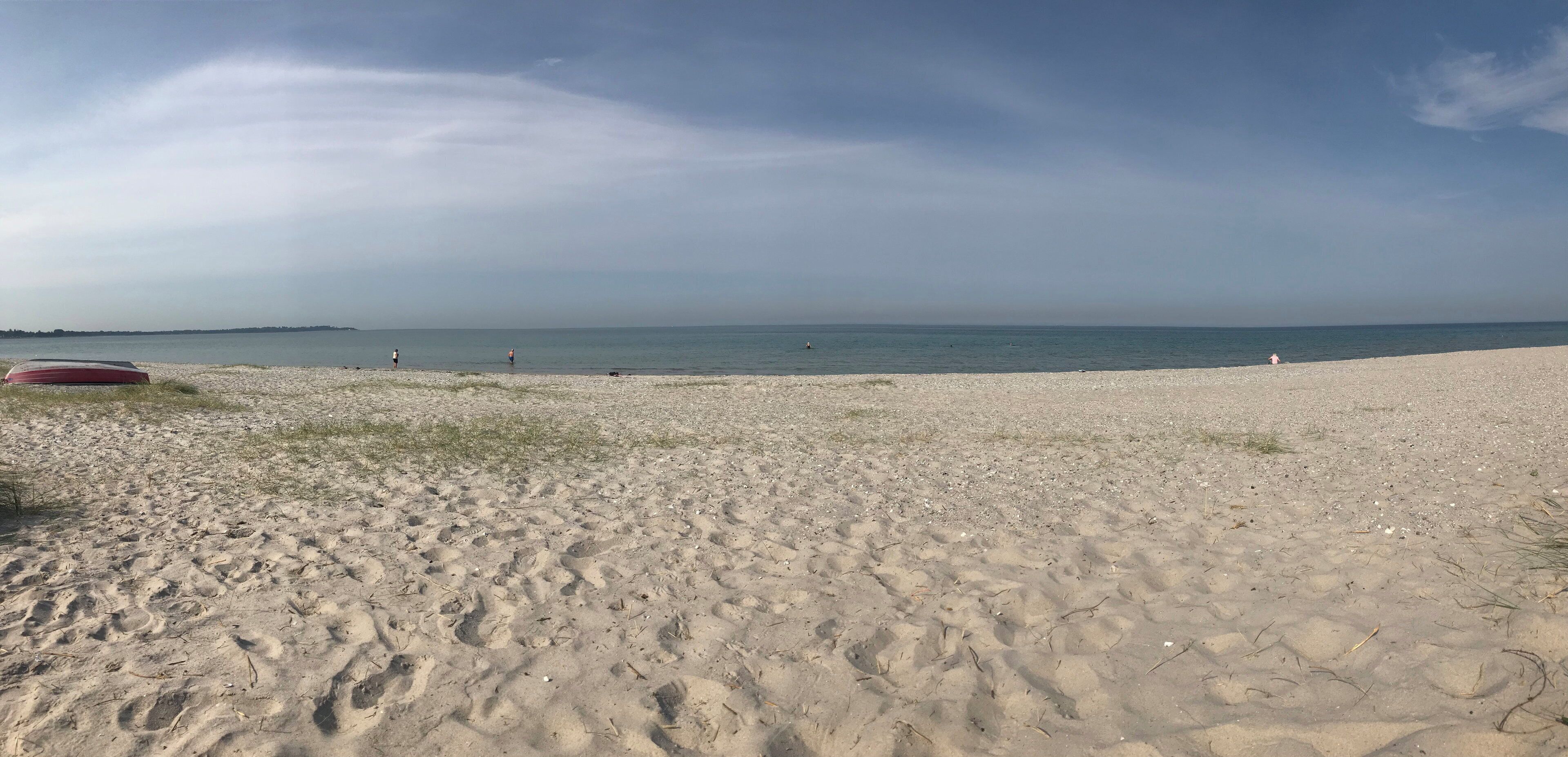 Une plage avec un bateau rouge, un ciel dégagé et une mer calme.