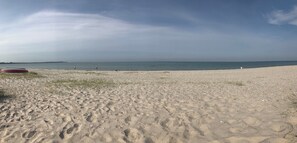Ein Strand mit einem roten Boot, blauem Himmel und ruhiger See.
