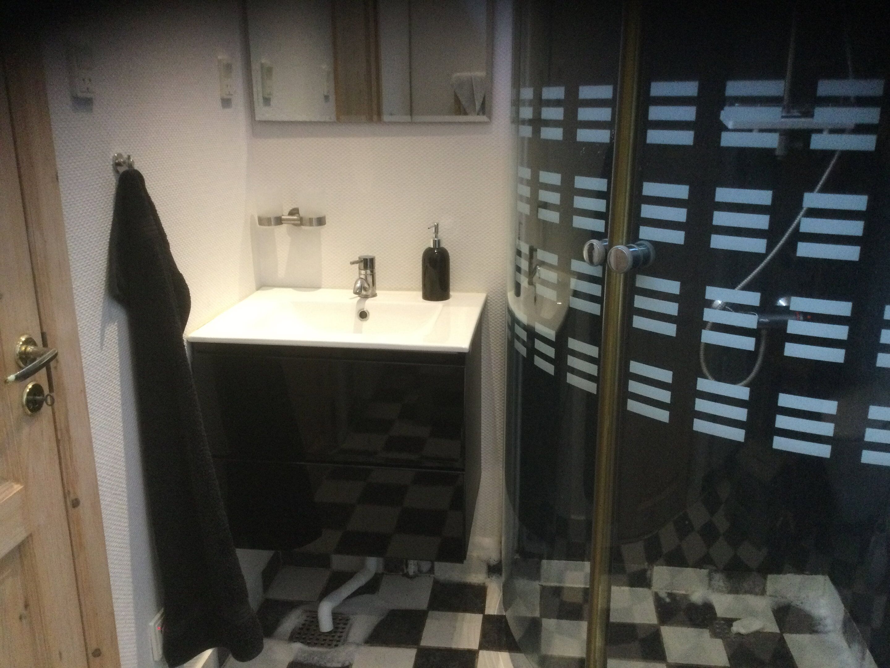 A bathroom with a checkered floor, a sink, a mirror, and a glass shower door.