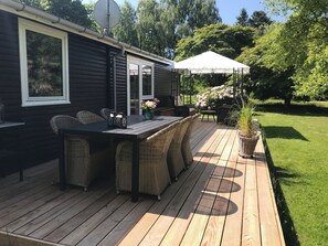 Een terras met een tafel en stoelen, een overdekt gedeelte met een witte parasol, en een tuin vol bloemen.