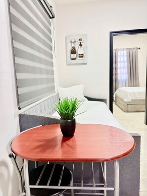 Een hotelkamer met een bed, een klein tafeltje met een plant, een raam met zonwering en een deur naar een andere kamer.