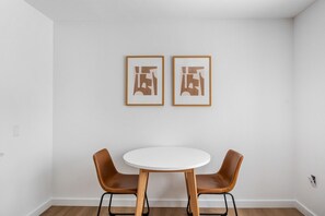 Ein Zimmer mit einem runden Tisch, zwei Stühlen, zwei gerahmten abstrakten Kunstwerken an der Wand und einer weißen Decke.