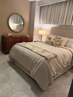 A bedroom with a large bed, a wooden dresser, a round mirror, and a window with curtains. - Located right on the water! Modern 1-bedroom condo in tranquil Mismaloya  (Mismaloya)